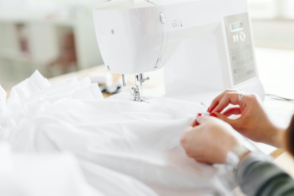 Cropped hands of fashion designer stitching white fabric sewing machine