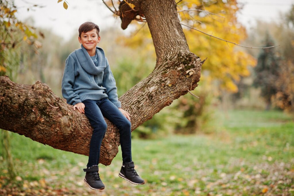Young boy sitting on tree at autumn park.